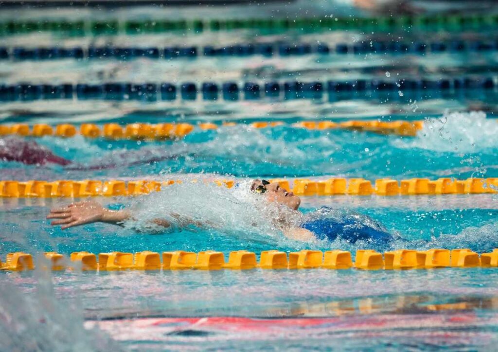 Nageur en action dans une piscine, bras tendu, eau en mouvement, lignes de séparation