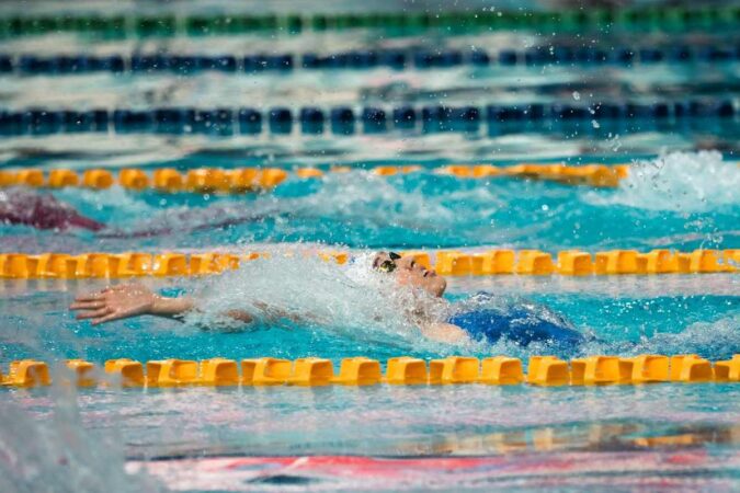 Nageur en action dans une piscine, bras tendu, eau en mouvement, lignes de séparation