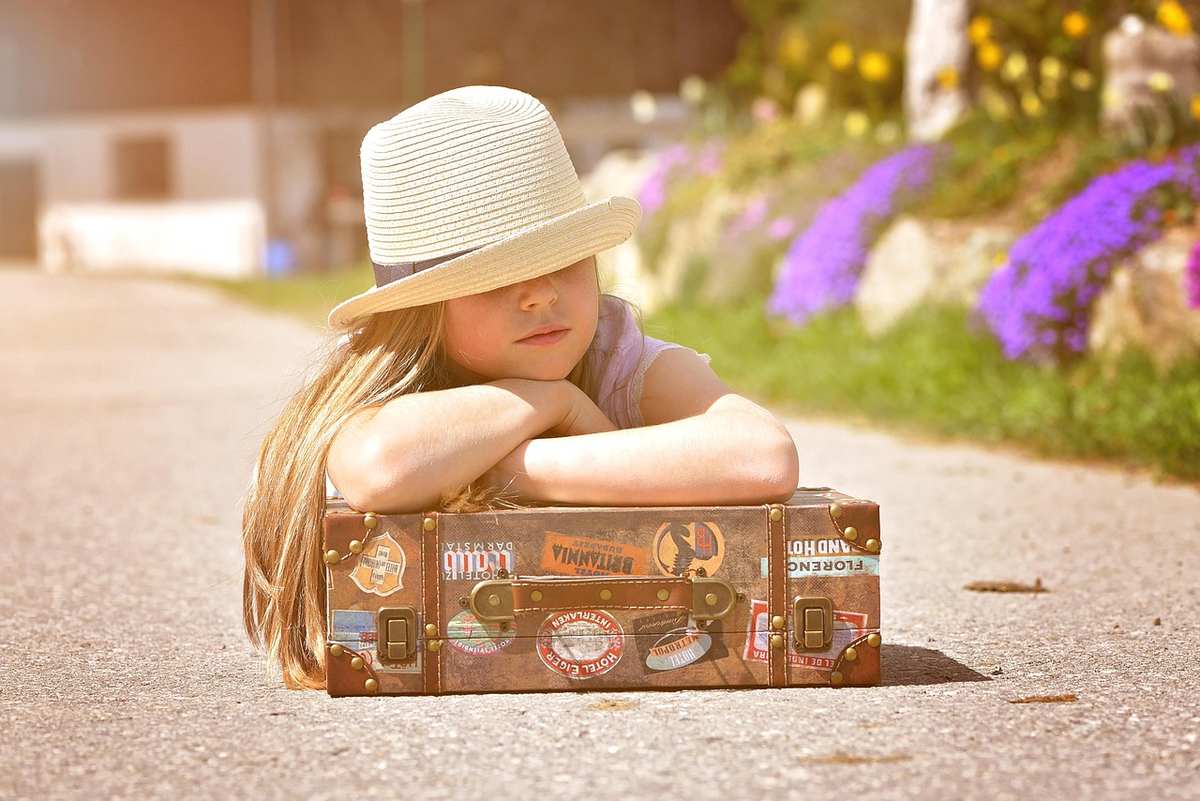 Une fillette en chapeau repose les bras sur une valise vintage Une fillette en chapeau repose les bras sur une valise vintage