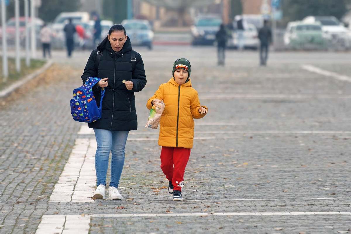Une femme portant un sac bleu accompagne un enfant en veste orange Une femme portant un sac bleu accompagne un enfant en veste orange