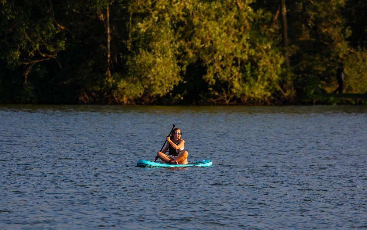 Une personne pratique le stand up paddle sur un lac calme entouré de forêt Une personne pratique le stand up paddle sur un lac calme entouré de forêt