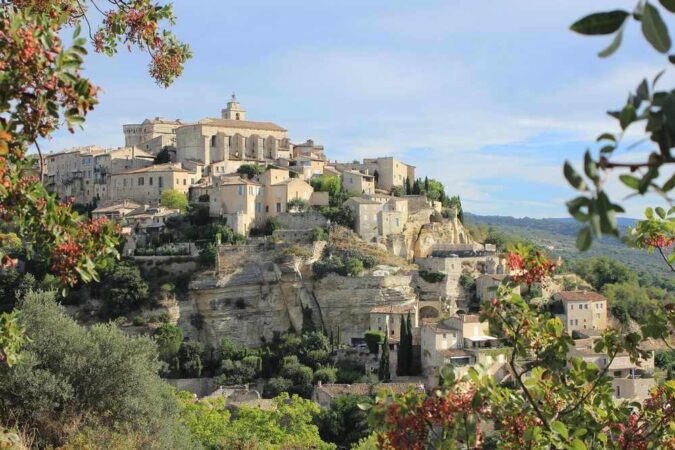 Village médiéval perché sur une colline, avec des bâtiments en pierre, des rues étroites, et une végétation luxuriante