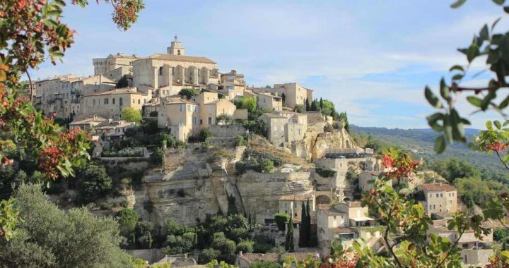 Village médiéval perché sur une colline, avec des bâtiments en pierre, des rues étroites, et une végétation luxuriante