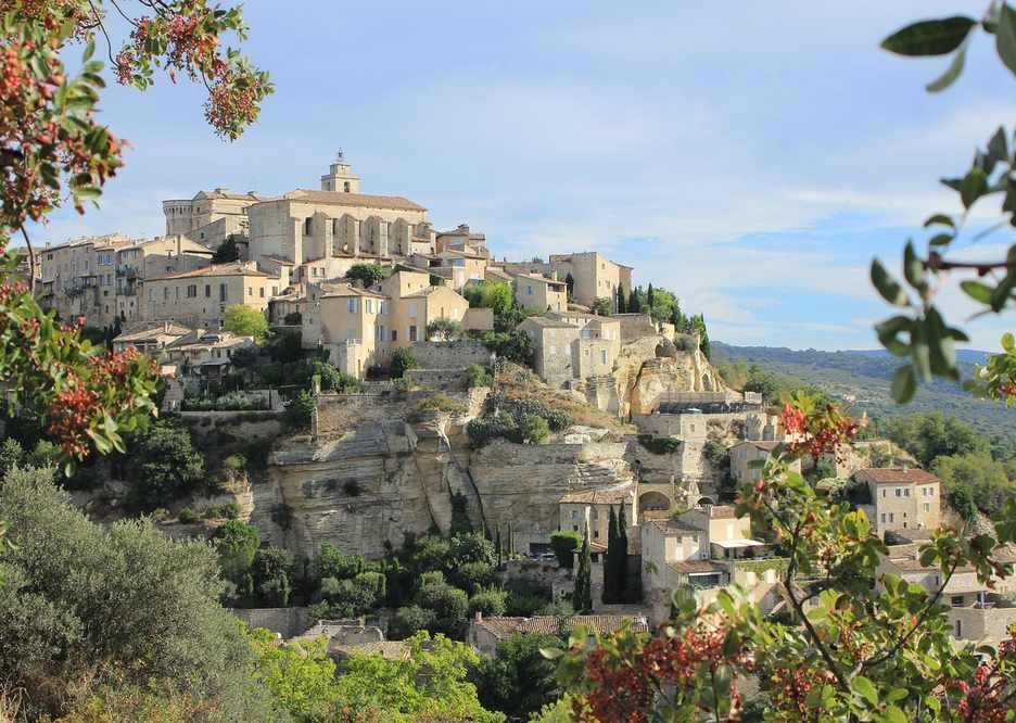 Village médiéval perché sur une colline, avec des bâtiments en pierre, des rues étroites, et une végétation luxuriante