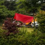 Voile rouge drapé sur un camping-car, entouré de verdure et d'arbres