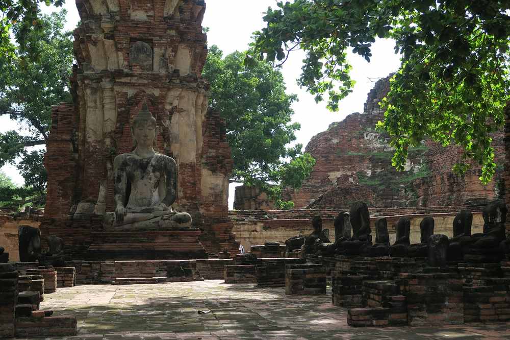 Statue de Bouddha assise au sein de ruines anciennes entourées d'arbres verts Statue de Bouddha assise au sein de ruines anciennes entourées d'arbres verts
