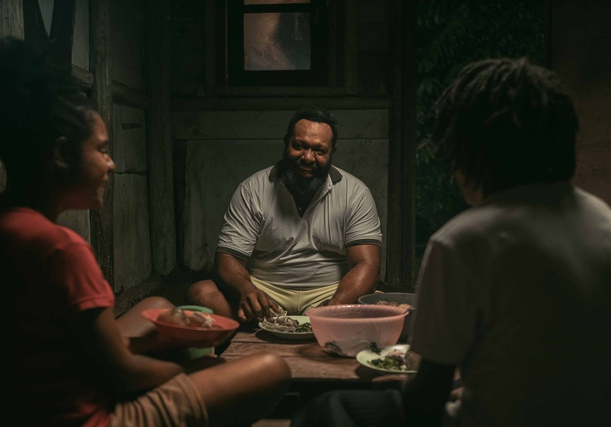 Famille noire partageant un repas dans une pièce sombre, expressions joyeuses Famille noire partageant un repas dans une pièce sombre, expressions joyeuses