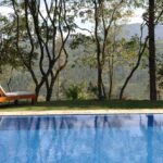 Une piscine bleue entourée de transat, arbres et montagne
