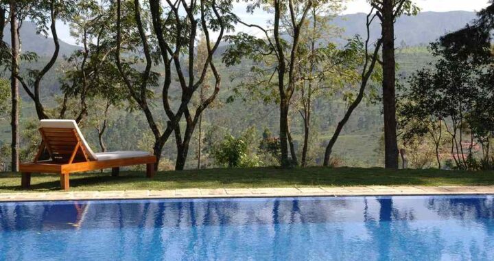 Une piscine bleue entourée de transat, arbres et montagne