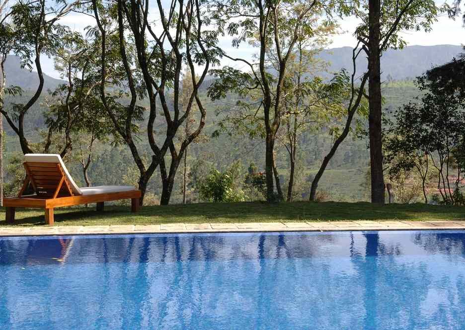 Une piscine bleue entourée de transat, arbres et montagne