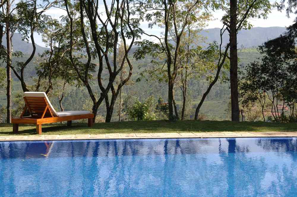 Une piscine bleue entourée de transat, arbres et montagne