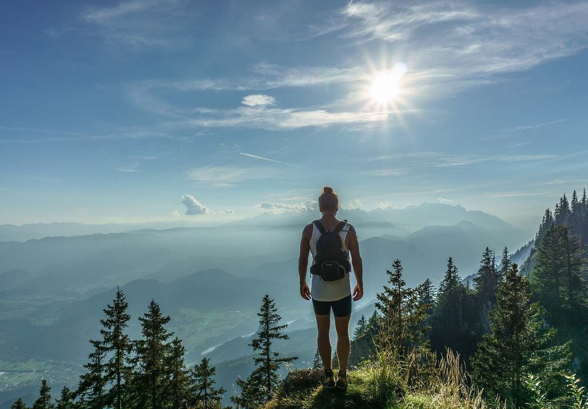 Une randonneuse solitaire admire le soleil au-dessus des montagnes et forêts Une randonneuse solitaire admire le soleil au-dessus des montagnes et forêts