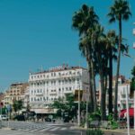 Une rue animée avec des palmiers, un grand hôtel et des voitures