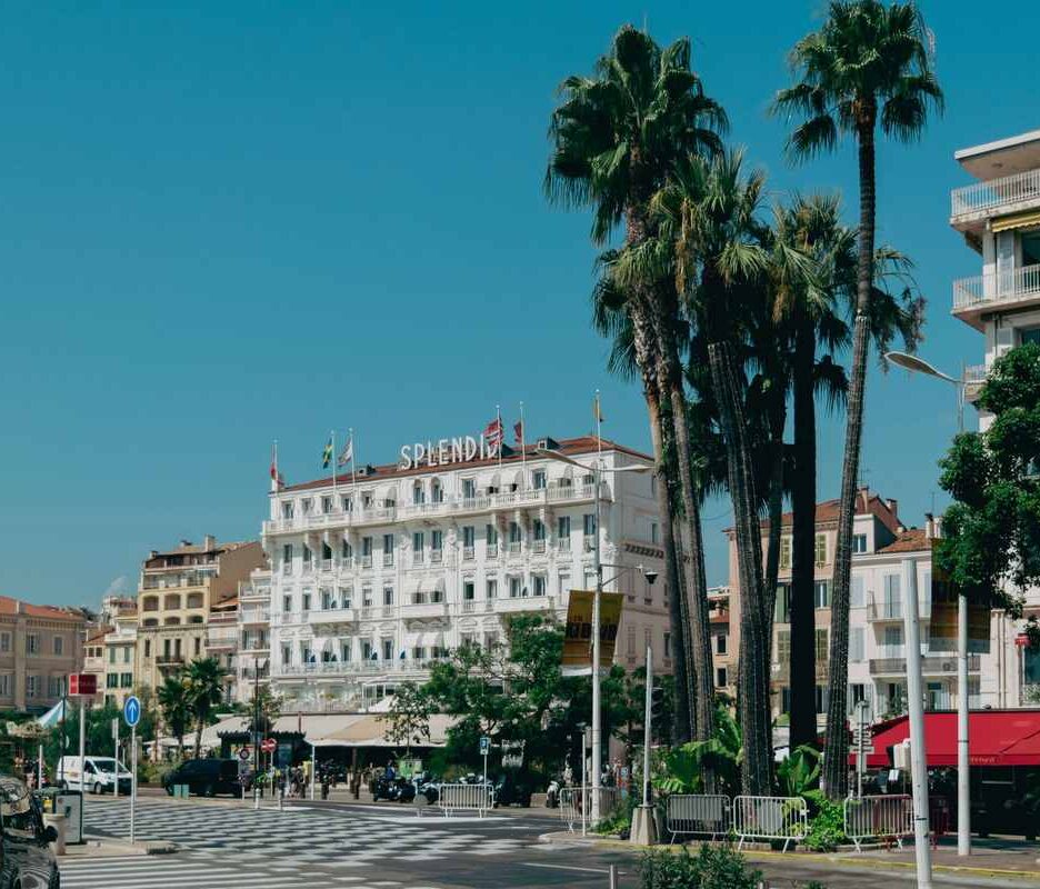 Une rue animée avec des palmiers, un grand hôtel et des voitures